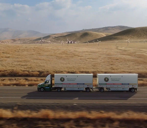 Old Dominion LTL truck driving through open countryside with wind turbines in the background.